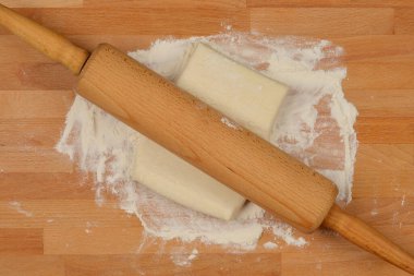 Ahşap bir merdane, ortasında küçük bir puf böreği hamuru dikdörtgeni olan un ahşap bir yüzey boyunca uzanır.