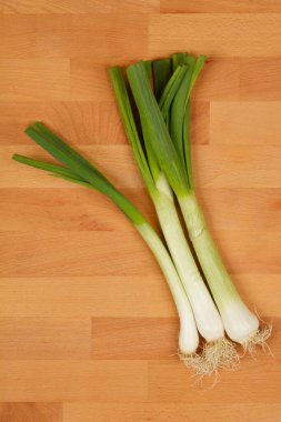 Tahta bir yüzeyde köşegen üzerinde üç taze soğanın yüksek açılı çekimi yeşil ve beyaz renklerini ve ince şekillerini gözler önüne seriyor.