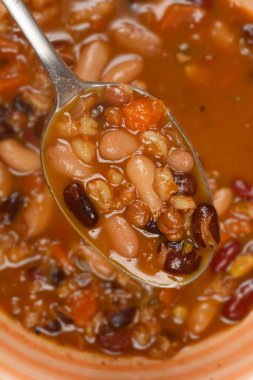 Bir kaşık dolusu fasulye yahnisinin yakın çekim, zengin bir et suyundaki fasulye ve sebzelerin çeşitliliğini gösteriyor.