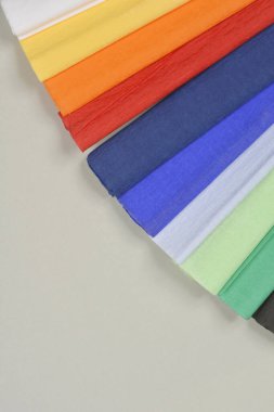 A close-up, angled shot of colorful crepe paper sheets arranged in a diagonal pattern, showcasing their vibrant hues and delicate texture against a neutral background