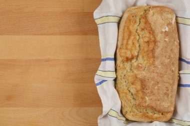 A top-down shot of a rustic loaf of sunflower seed bread on a striped cloth, beside a wooden surface, highlighting its homemade texture