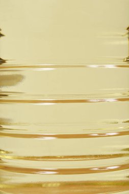 An extreme close-up shot of the textured surface of a clear plastic bottle filled with yellow cooking oil, highlighting the bottle's ribbing