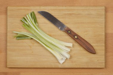 Dilimlenmiş yeşil soğan ve tahta kesme tahtasına saplanmış bir bıçak.