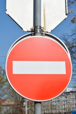 Metal bir direğe bağlı yatay beyaz çubuklu kırmızı ve beyaz yol tabelasının yakın plan görüntüsü. Ağaçların ve mavi gökyüzünün arka planına karşı.
