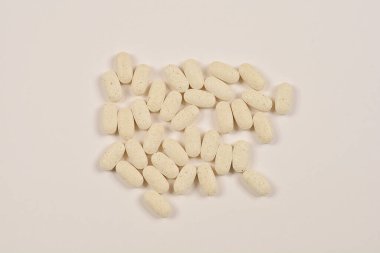 Açık gri bir yüzeye saçılmış oval şekilli beyaz hapların yukarıdan aşağı görüntüsü.