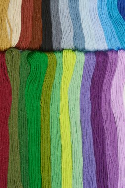 Paralel satırlarda düzenlenmiş çeşitli renkli nakış ipliklerinden oluşan yakın plan bir fotoğraf. Renklerin canlı bir spektrumunu gösteriyor.