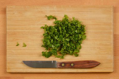 Tahta bir kesme tahtasının üzerinde küçük bir bıçakla doğranmış maydanozdan yapılmış tepeden tırnağa bir kare taze otlar aşçılık için hazır.