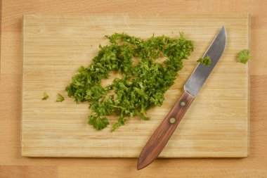 Tahta bir kesme tahtasının üzerinde küçük bir bıçakla doğranmış maydanozdan yapılmış tepeden tırnağa bir kare taze otlar aşçılık için hazır.
