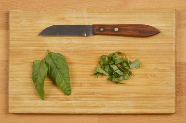 Taze fesleğen yaprakları, biraz bütün ve biraz da doğranmış, küçük tahta saplı bir bıçağın yanına konur.