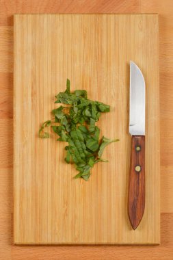 Taze kesilmiş fesleğen yaprakları hafif bir tahta kesme tahtasının üzerine küçük bir bıçağın yanına yerleştirilir.