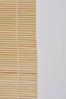 Geleneksel bambu suşi hasırının minimalist, yakın plan bir görüntüsü. Temiz, hafif bir zemin üzerinde yuvarlanan, dokusunu ve tasarımını ön plana çıkaran.