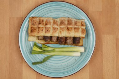 Mavi tabakta yeşil soğanlı bir ekmeğin içinde doğranmış et parmakları (cevapi).