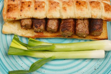 Mavi tabakta yeşil soğanlı bir ekmeğin içinde doğranmış et parmakları (cevapi).