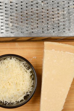 Bir kasede ızgara parmesan peyniri, bir parça parmesan peyniri, ve tahta tahtada bir rende, yukarıdan atılmış.