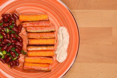Bir sıra ızgara surimi çubuğu, bir parça kremalı sos ve yanında kırmızı fasulye salatası olan tabağın yukarıdan görünüşü.