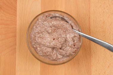 İçi çikolatalı tatlıyla dolu, içi açık ahşap bir yüzeye kurulmuş, kaşıkla dolu cam bir kasenin yukarıdan aşağı görüntüsü.