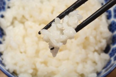 Pirinç, pişmiş tanelerin dokusuna ve detaylarına odaklanarak, siyah çubukların arasında tutulur.