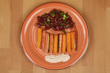 Bir sıra ızgara surimi çubuğu, bir parça kremalı sos ve yanında kırmızı fasulye salatası olan tabağın yukarıdan görünüşü.