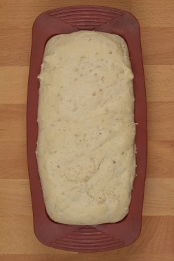 Pişmemiş ekmek hamuru, ahşap bir yüzey üzerinde kestane rengi silikon bir somun tavada oturur.