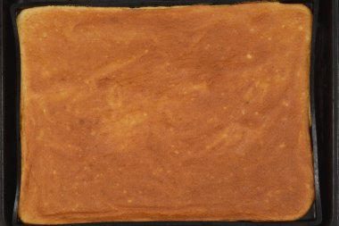 Yeni pişmiş altın sarısı bir sünger keki siyah bir tavada.