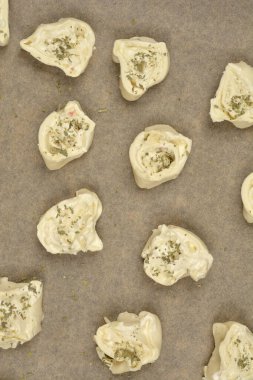 Tepeden çekimde çiğ peynir ve kekikli börekler parşömen kağıdına konmuş, pişirilmeye hazır.