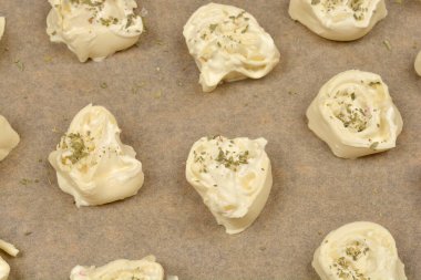 Tepeden çekimde çiğ peynir ve kekikli börekler parşömen kağıdına konmuş, pişirilmeye hazır.
