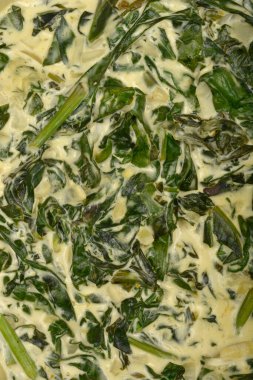 Yakın plan, yukarıdan aşağıya doğru çekimde kremalı ıspanak görünür yeşil yapraklar ve açık renkli sos var.