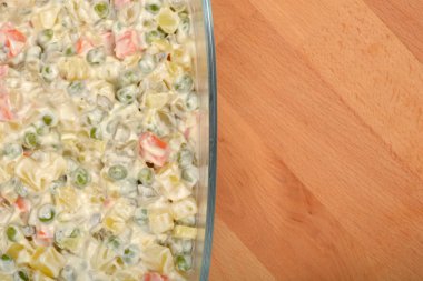 İçi kremalı Hırvat usulü Fransız salatasıyla dolu cam bir tabak. Görünür sebzeler ve mayonez, yukarıdan bakıldığında ahşap bir yüzeyde duruyor.