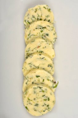 Soluk sarı tereyağı dilimleri yeşil otlar ve sarımsak ile dikey olarak beyaz bir tabakta dizilir, yukarıdan aşağıya doğru bir perspektiften yakalanır.