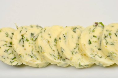 Soluk sarı tereyağı dilimleri yeşil otlar ve sarımsak ile dikey olarak beyaz bir tabakta dizilir, yukarıdan aşağıya doğru bir perspektiften yakalanır.