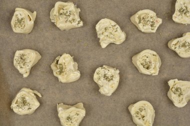Tepeden çekimde çiğ peynir ve kekikli börekler parşömen kağıdına konmuş, pişirilmeye hazır.