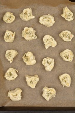 Tepeden çekimde çiğ peynir ve kekikli börekler parşömen kağıdına konmuş, pişirilmeye hazır.