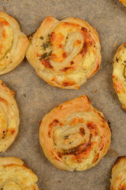 Üzerinde altın esmer peynirli puf börekleri olan bir fotoğraf. Parşömen kağıdına yerleştirilmiş.