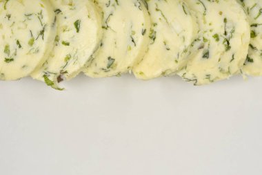 Soluk sarı tereyağı dilimleri yeşil otlar ve sarımsak ile beyaz bir tabakta dizilir, yukarıdan aşağıya doğru bir perspektiften yakalanır.