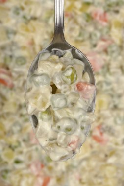 Bir kaşık dolusu kremalı Hırvat usulü sebzeli ve mayonezli Fransız salatası kalan salatanın üzerinde bulanık bir arka planda tutuluyor.