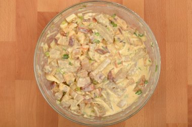 Yukarıdan bakıldığında, açık kahverengi ahşap bir yüzeye kurulmuş, içinde küp ekmek, sebze ve peynir bulunan, açık kahverengi bir cam kase görülüyor.