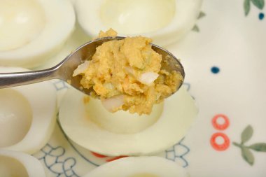 Yakın plan, bir kaşık dolusu kremalı açık sarı dolgu gösteriyor. Yumurta sarısı, avokado ve soğan püresi ile yapılmış. Yarım yamalak, kaynamış bir yumurtaya yerleştiriliyor.