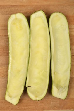 Üç yarıya bölünmüş ve kepçelenmiş kabak, açık kahverengi ahşap bir yüzey üzerinde dikey olarak sıralanır.