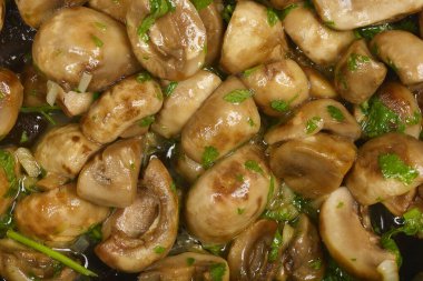 Yakın plan çekimde sosla parlayan sotelenmiş mantarlar ve taze bitkiler serpiştirilmiş.