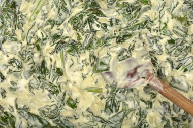 Yakın çekim, kremalı yeşil ıspanağın tahta kaşıkla karıştırıldığını gösteriyor.