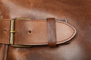 Yakından bakınca kahverengi deri bir kayış görünüyor. Üzerinde pirinç toka var. Koyu kahverengi deri bir yüzey.