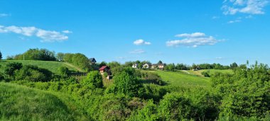 Gornje Psarthe 'nin doğuya bakan manzarası, dağınık bulutlu, mavi gökyüzünün altında evleri olan yuvarlanan yeşil tepeleri ortaya çıkarıyor.