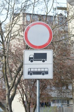 Araç ve otobüsler için giriş olmadığını gösteren bir trafik işareti, ağaçların ve binanın bulanık arkaplanına karşı duruyor