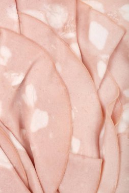 Yakın plan çekimde, mortadella 'nın üst üste binen ince dilimleri, soluk pembe rengini ve karakteristik beyaz yağ içeriklerini gözler önüne seriyor.