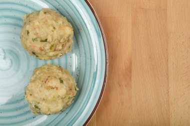 Tepeden çekimde, ahşap arka planda mavi bir seramik tabağa yerleştirilmiş yeşil bitkilerle pişirilmiş iki ekmek köftesi görülüyor.
