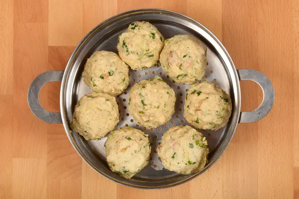 Tahta bir yüzey üzerinde pişirilmeye hazır metal bir buhar tenceresine konmuş otlu ekmek hamuru.