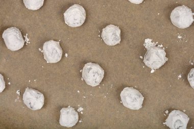 Pudra şekeri tozlu, çikolatalı, kırışık kurabiyeler açık kahverengi bir tepside pişirilmeye hazırdır.