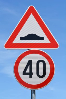 Mavi gökyüzüne karşı iki belirgin yol işareti: bir hız tümseği için kırmızı kenarlı üçgen uyarı işareti ve 40 km / saat hız limitini gösteren kırmızı kenarlı dairesel tabela