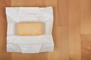 Yukardan aşağı doğru beyaz kağıttan kısmen açılmış bir dilim Limburger peyniri, sıcak ahşap bir yüzey üzerinde dinleniyor.