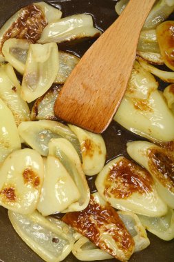 Tahta bir spatula, açık yeşil çan biberi dilimlerini karıştırır. Koyu bir tavada kahverengileşir. Bu da pişirildiklerini gösterir.